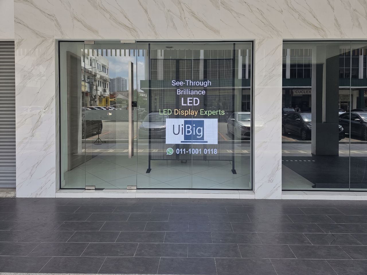 UiBig's transparent LED display on a live glass shopfront reading 'See-Through Brilliance — LED Display Experts', clear from the street in daylight